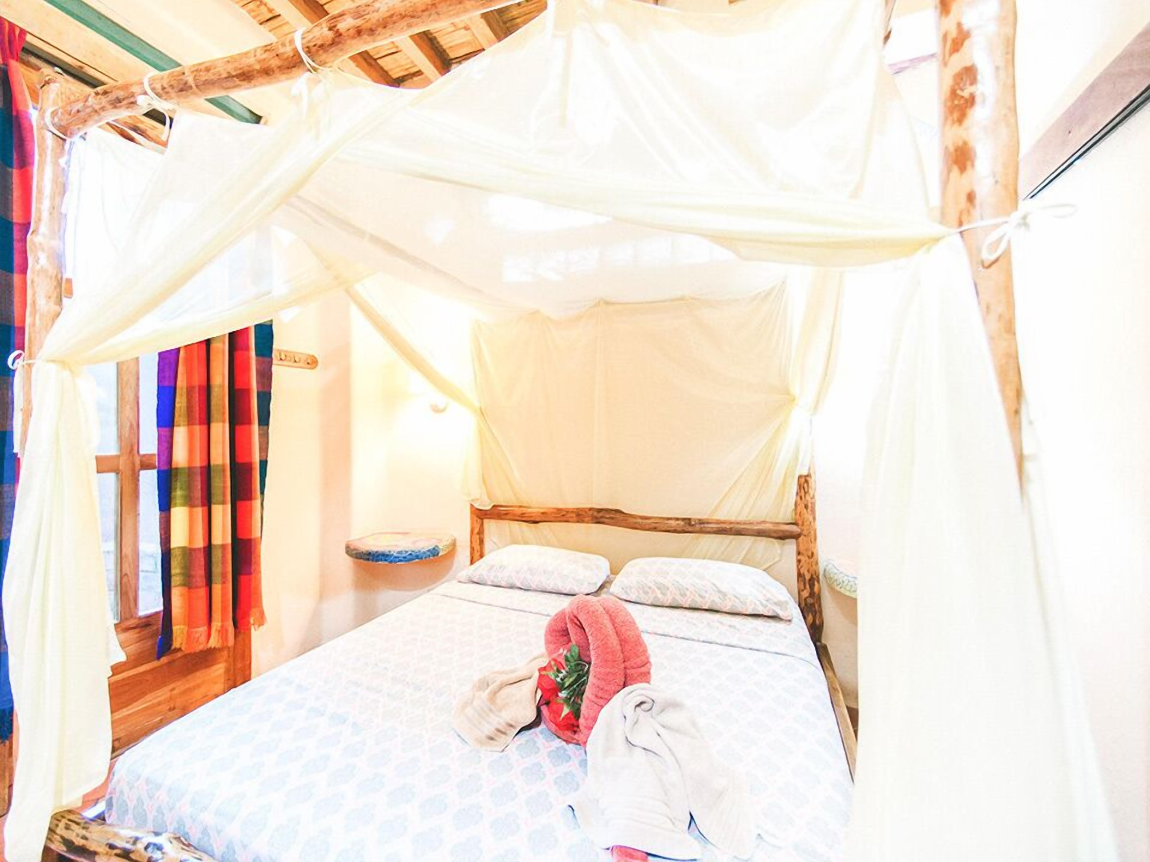 Una cama con dosel, una mesita de noche y una ventana con cortinas.