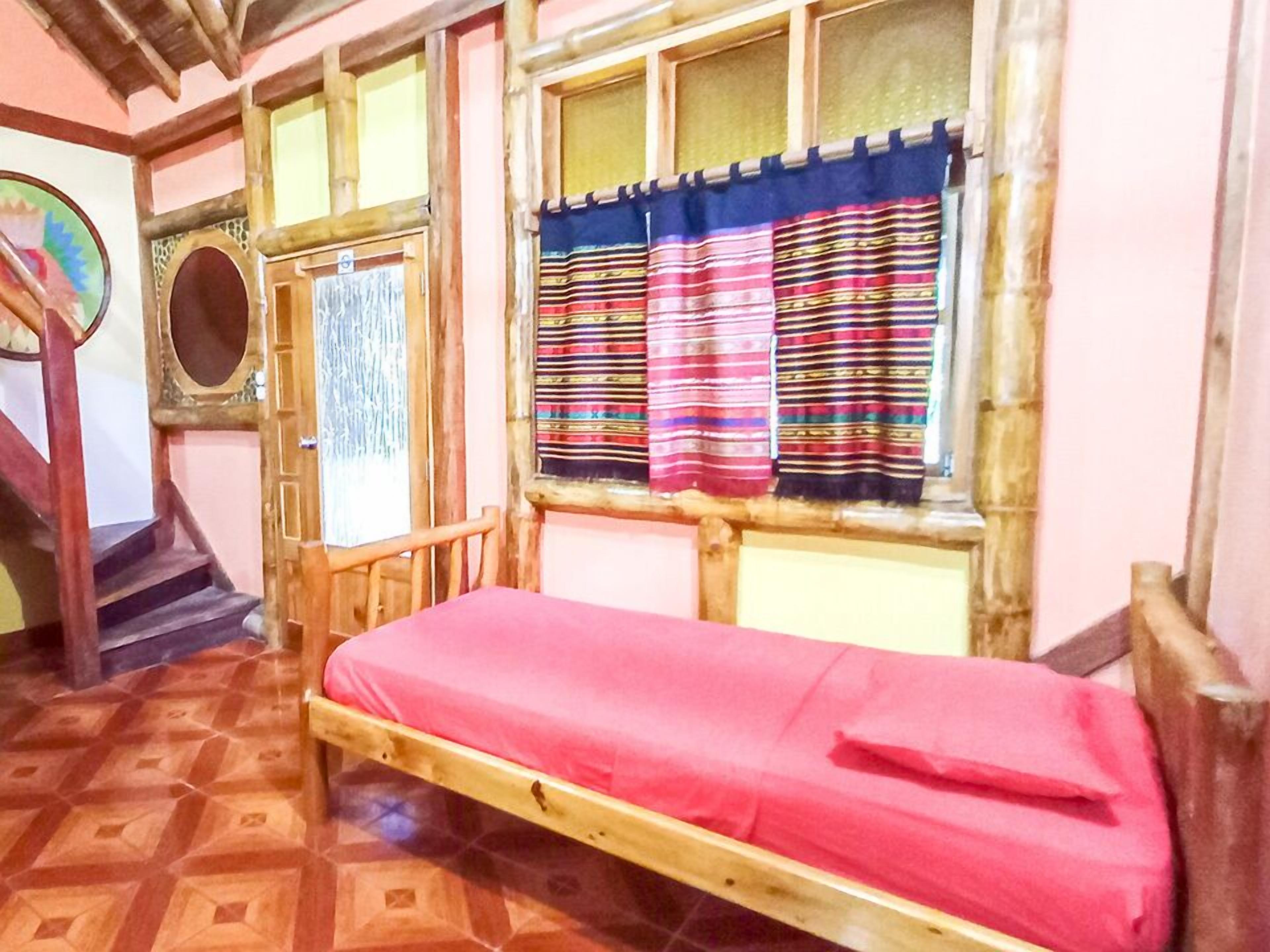 A room with a wooden bed, a staircase, and a window with striped curtains.
