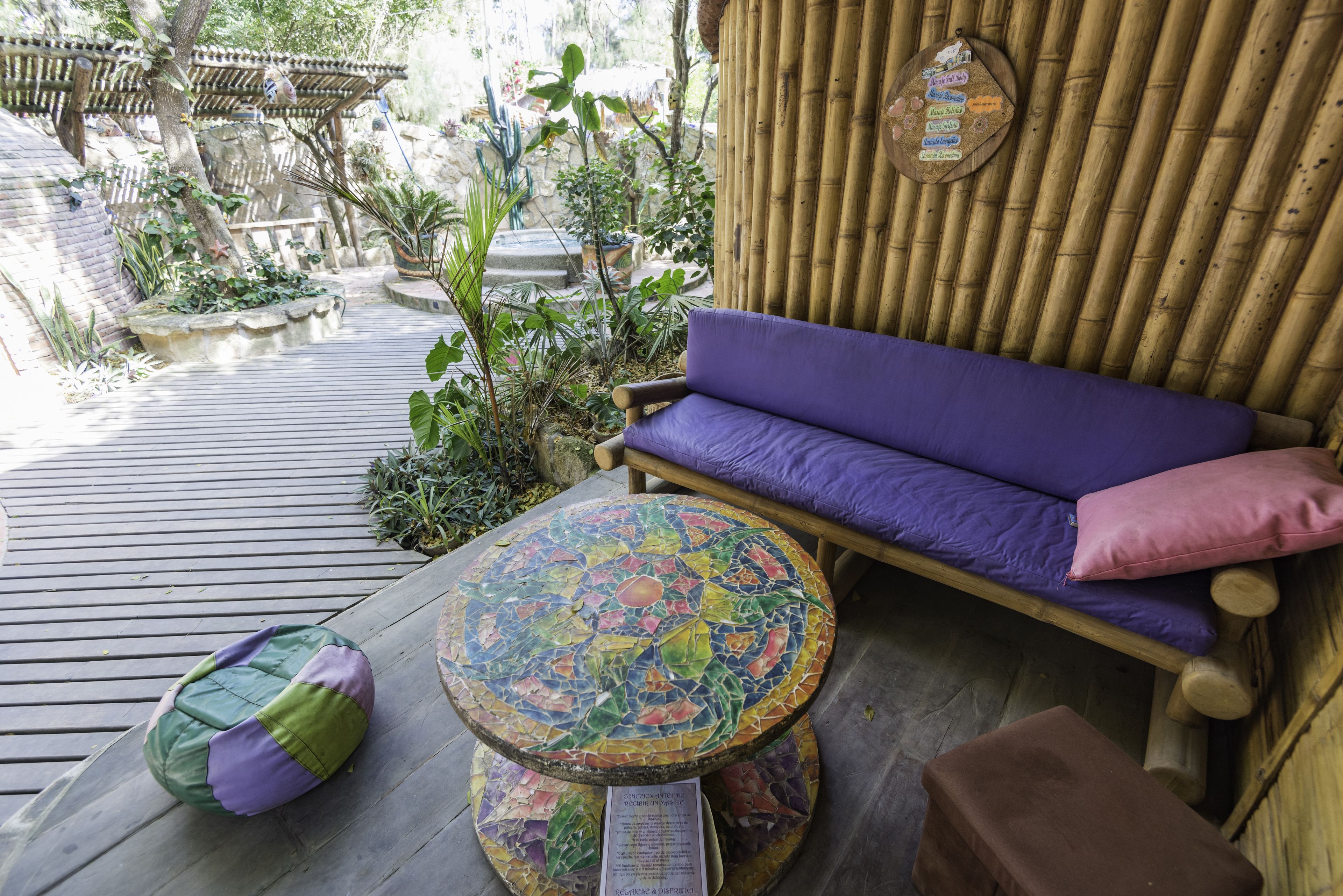 A wooden deck with a purple sofa, a mosaic table, and a wooden bench.