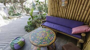 A wooden deck with a purple sofa, a mosaic table, and a wooden bench.
