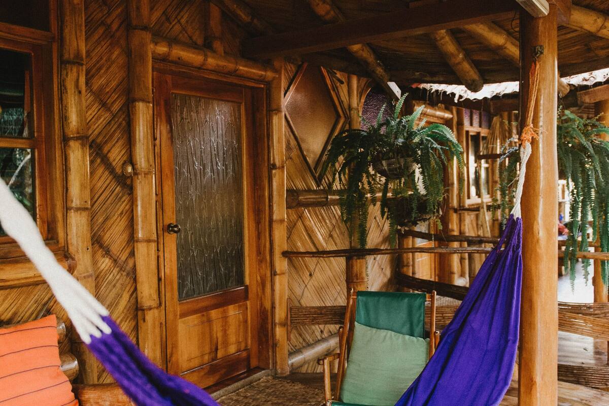 A wooden cabin with a hammock, a green chair, and a wooden door.
