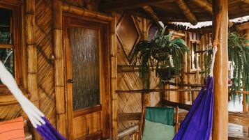 A wooden cabin with a hammock, a green chair, and a wooden door.