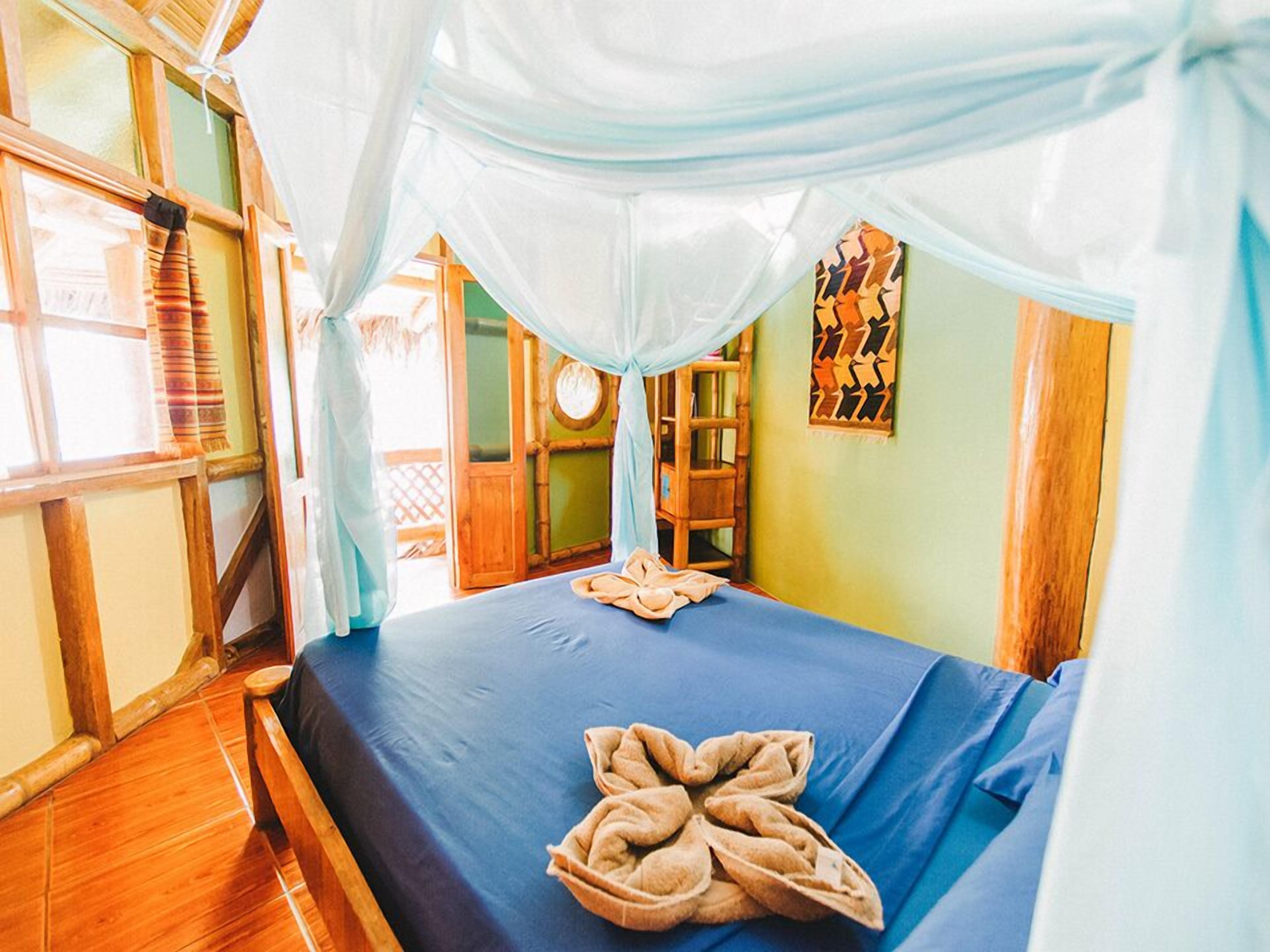 A room with a bed under a canopy, a wooden floor, and a view of the outside.