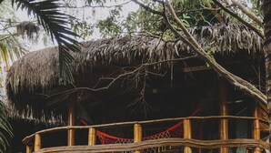 Una estructura de bambú de dos pisos con techo de paja, rodeada de vegetación tropical.