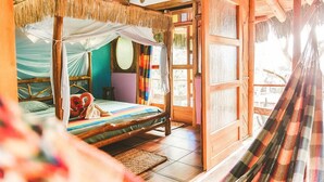 Una habitación con cama bajo techo de paja, una hamaca y vistas al exterior.