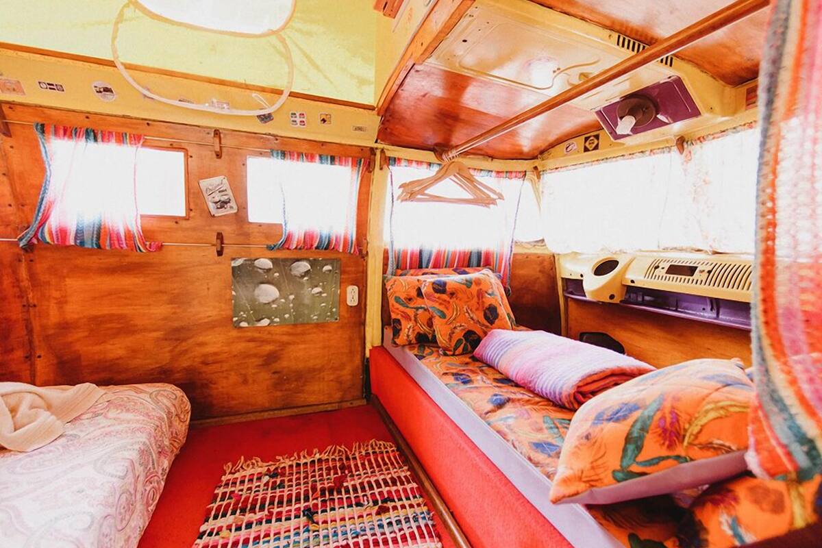 A cozy RV interior with a bed, a small table, and a window with curtains.