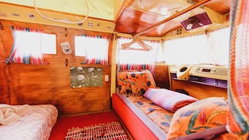 Interior acogedor de una caravana con cama, una mesita y una ventana con cortinas.