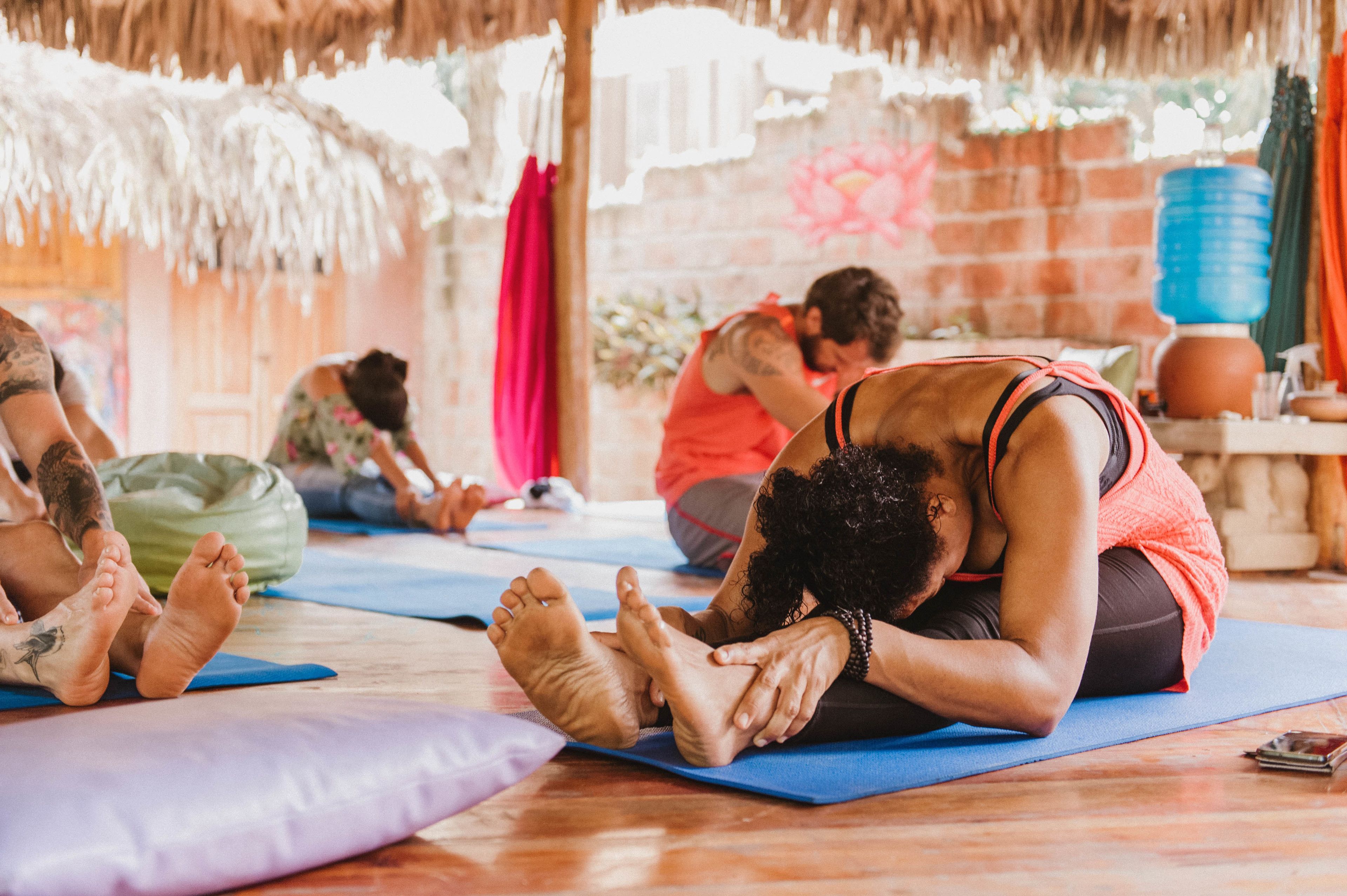 A group of people on yoga mats in a room with a brick wall and a thatched roof.