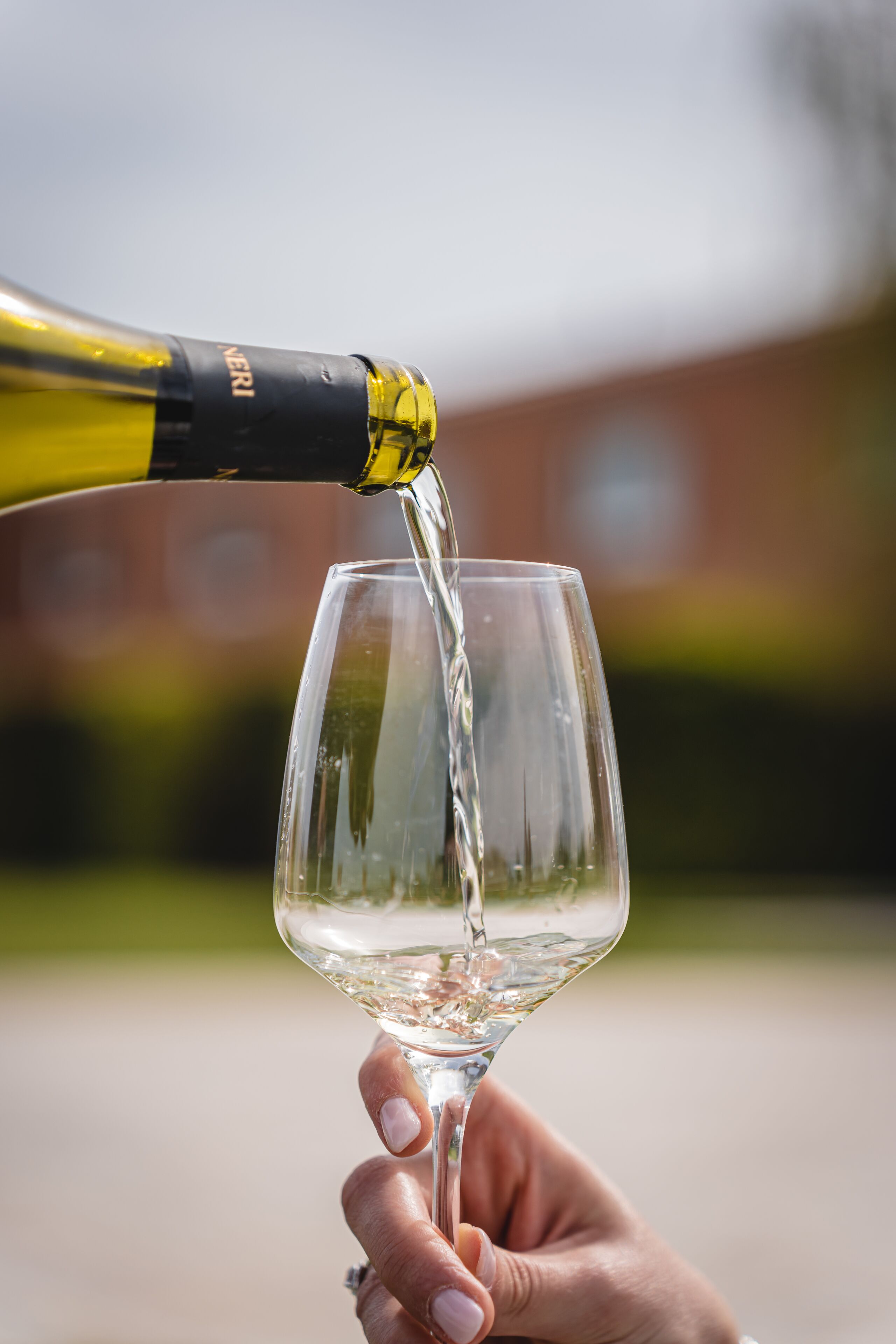 A hand holding a wine glass with white wine being poured into it.