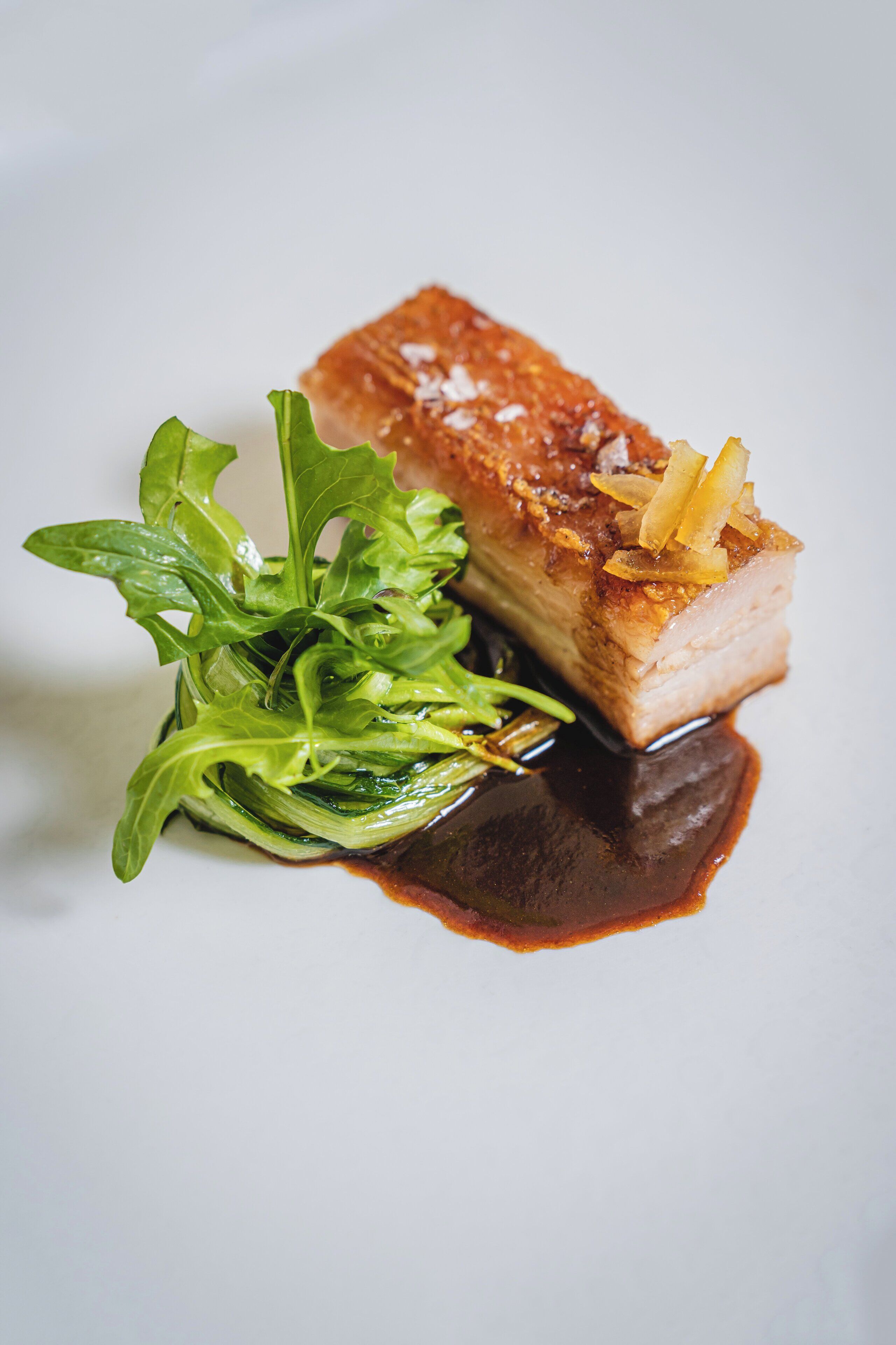A dish with a piece of meat, greens, and sauce on a plate.