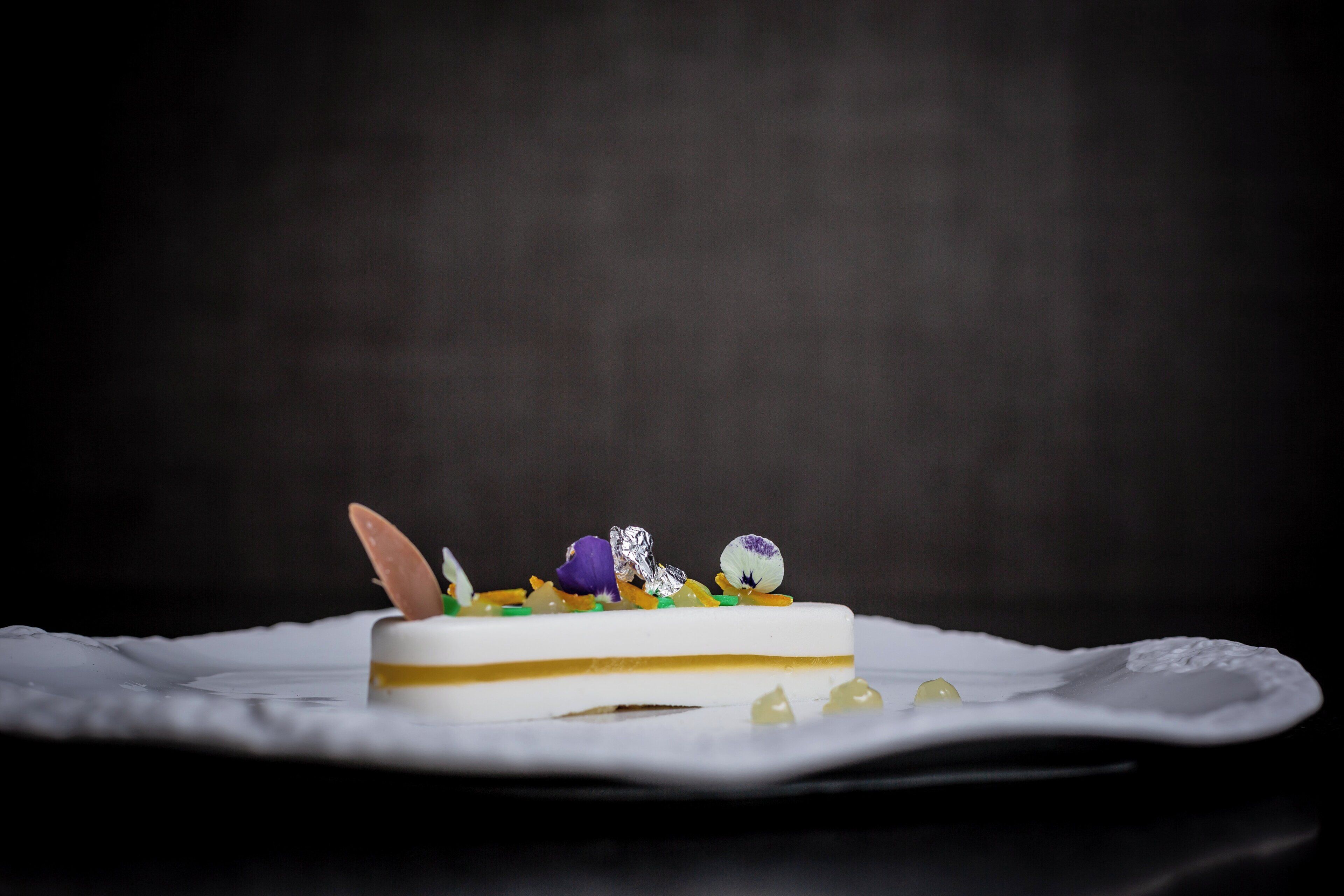 Ein Dessert mit weißer Basis, einer goldenen Schicht und Dekorationen auf einem weißen Teller.