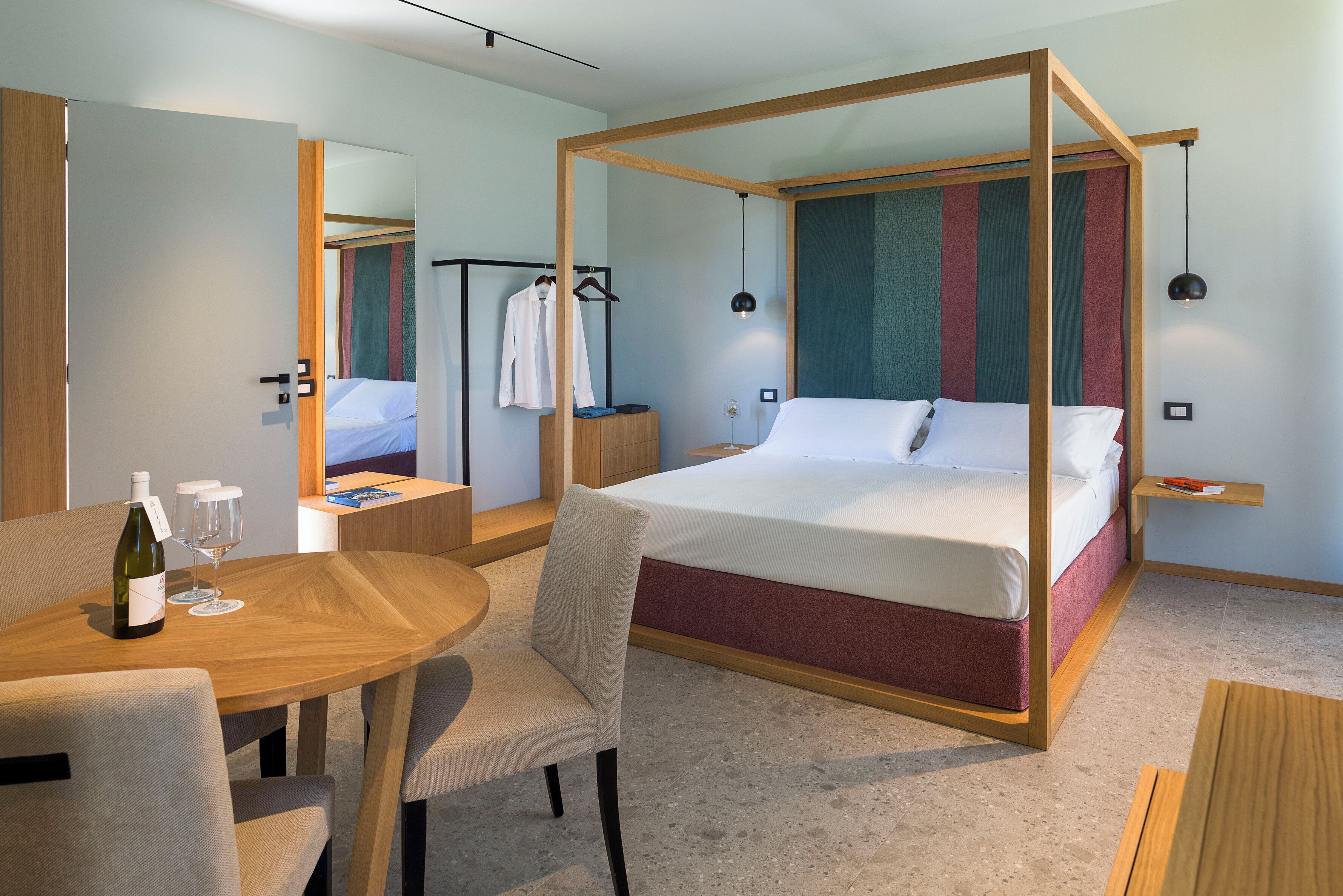 Et moderne hotelværelse med himmelseng, et træbord med to vinglas og en flaske, samt et spejl på væggen.