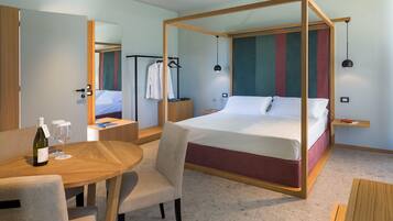 A modern hotel room with a four-poster bed, a wooden table with two wine glasses and a bottle, and a mirror on the wall.