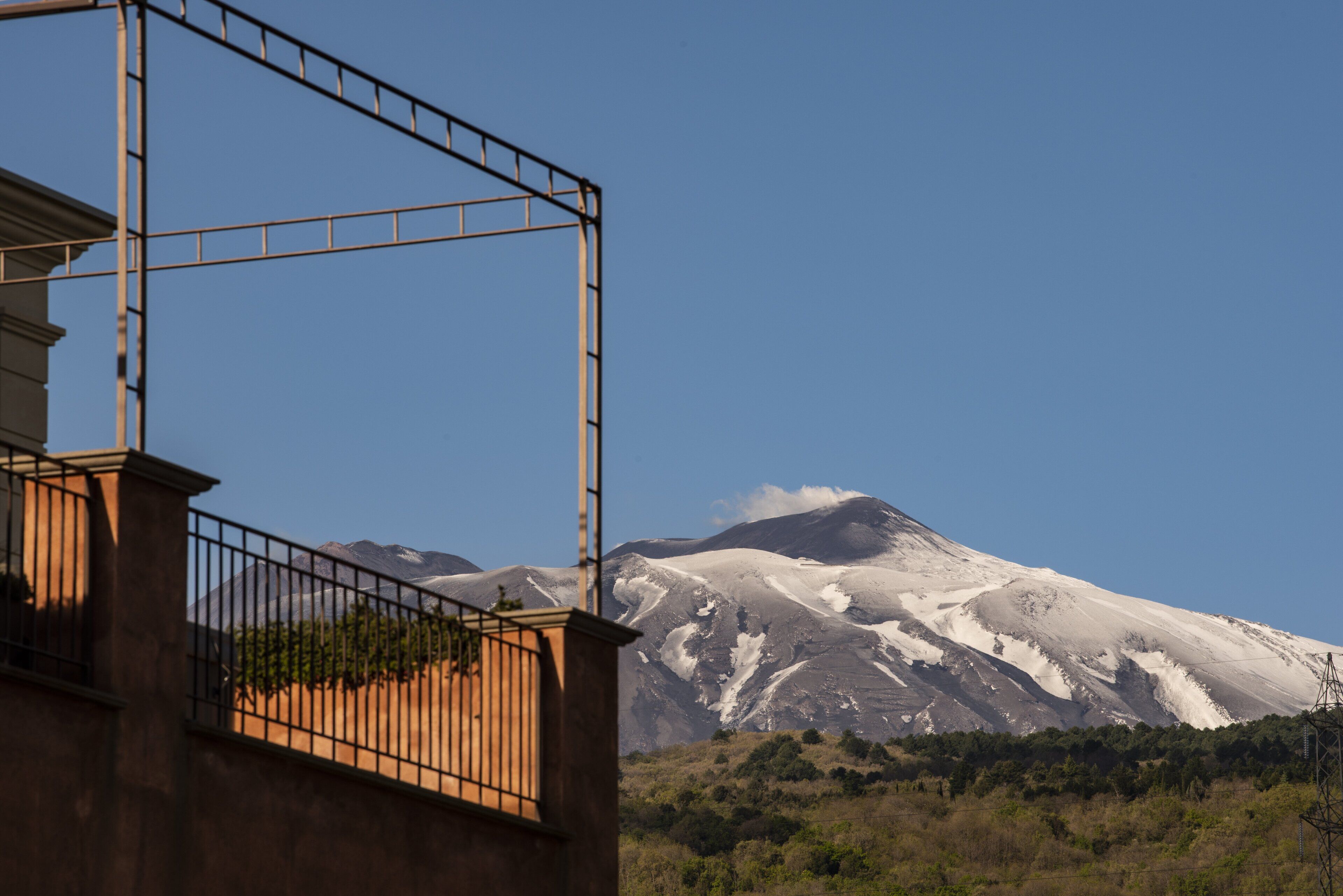 Ein Berg mit schneebedeckten Gipfeln, einem klaren Himmel und einem Gebäude mit Balkon und Geländer.