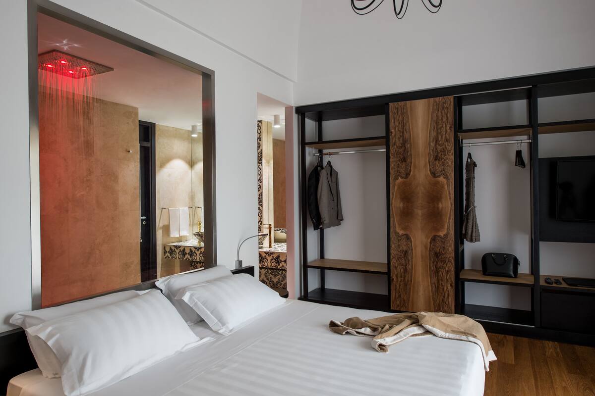 A modern hotel room with a large bed, a wooden wardrobe, and a mirror.