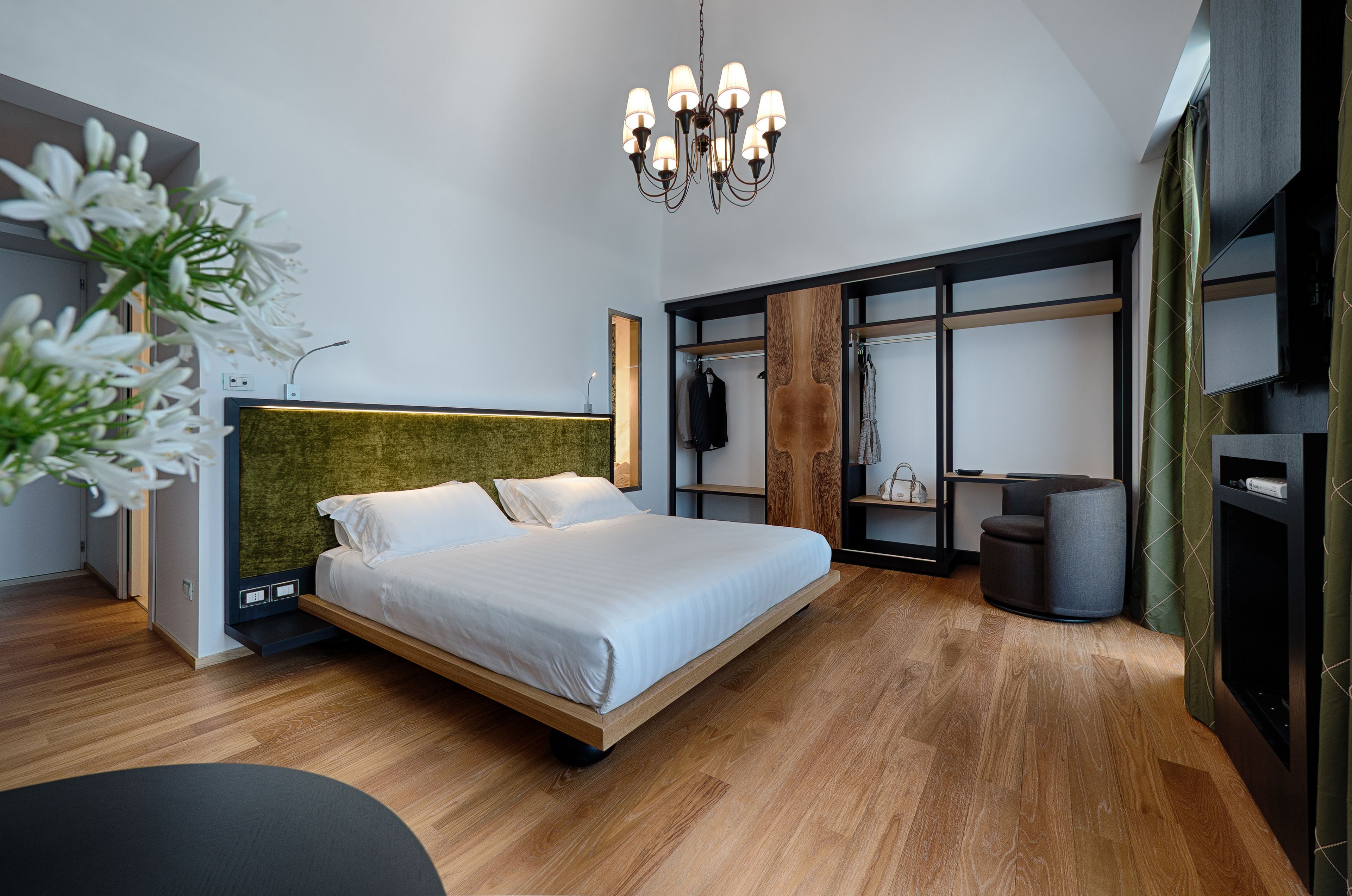 A modern bedroom with a large bed, a wooden headboard, a built-in wardrobe, and a chandelier.