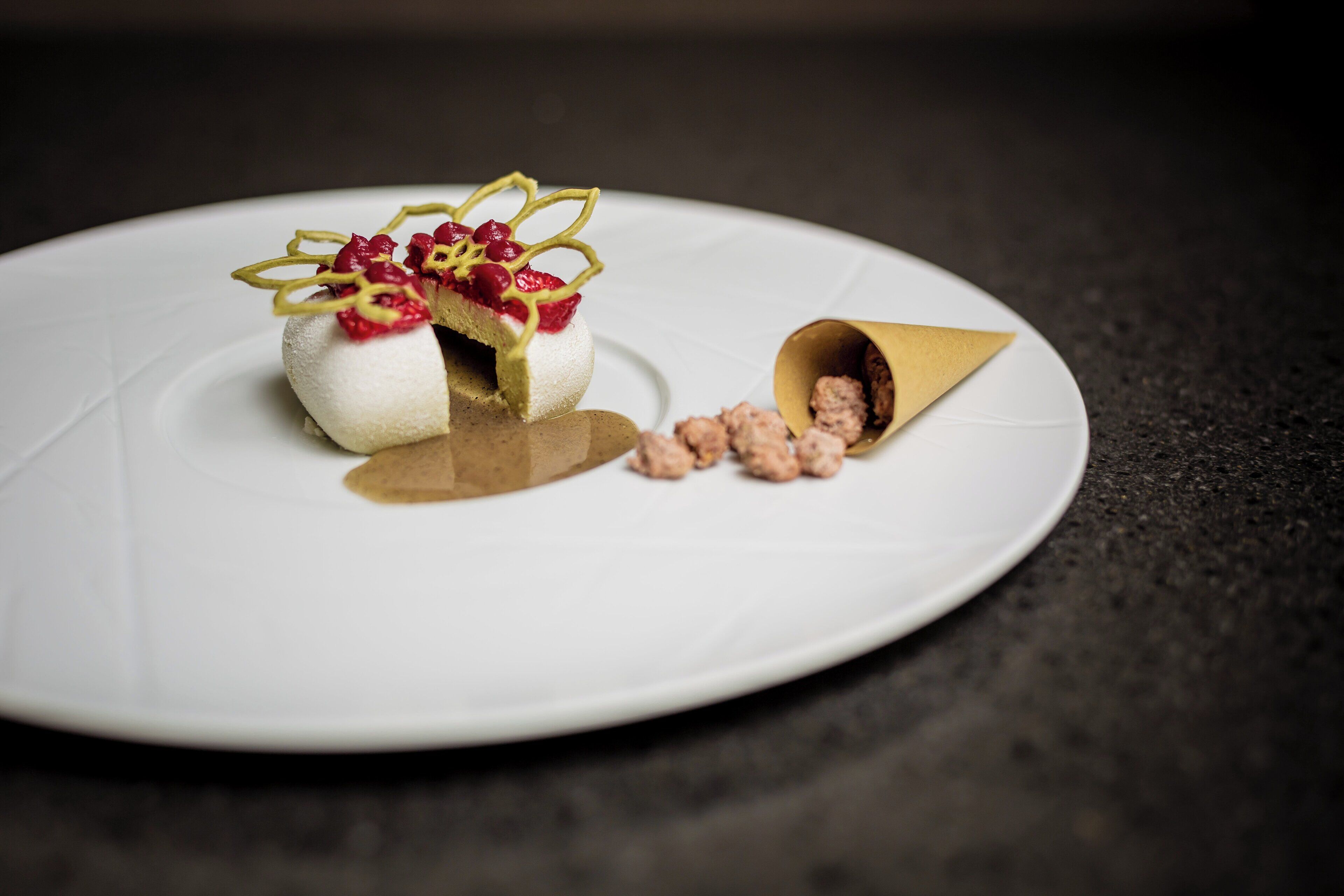 Un postre sobre un plato blanco con una cuchara dorada y algunas nueces a un lado.
