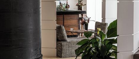 A modern living room with a large black column, a brown sofa, a patterned armchair, and a potted plant.