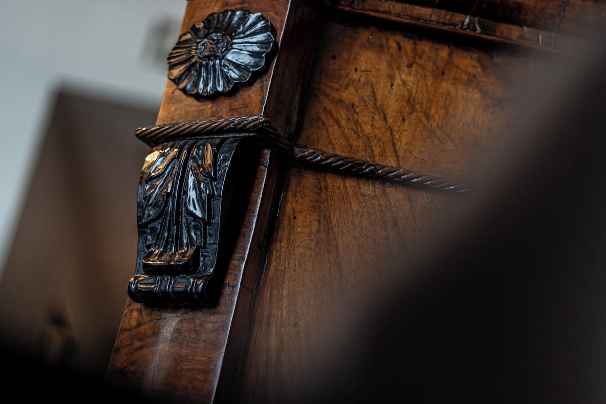 A close-up of a wooden chair with carved details and a metal chain.