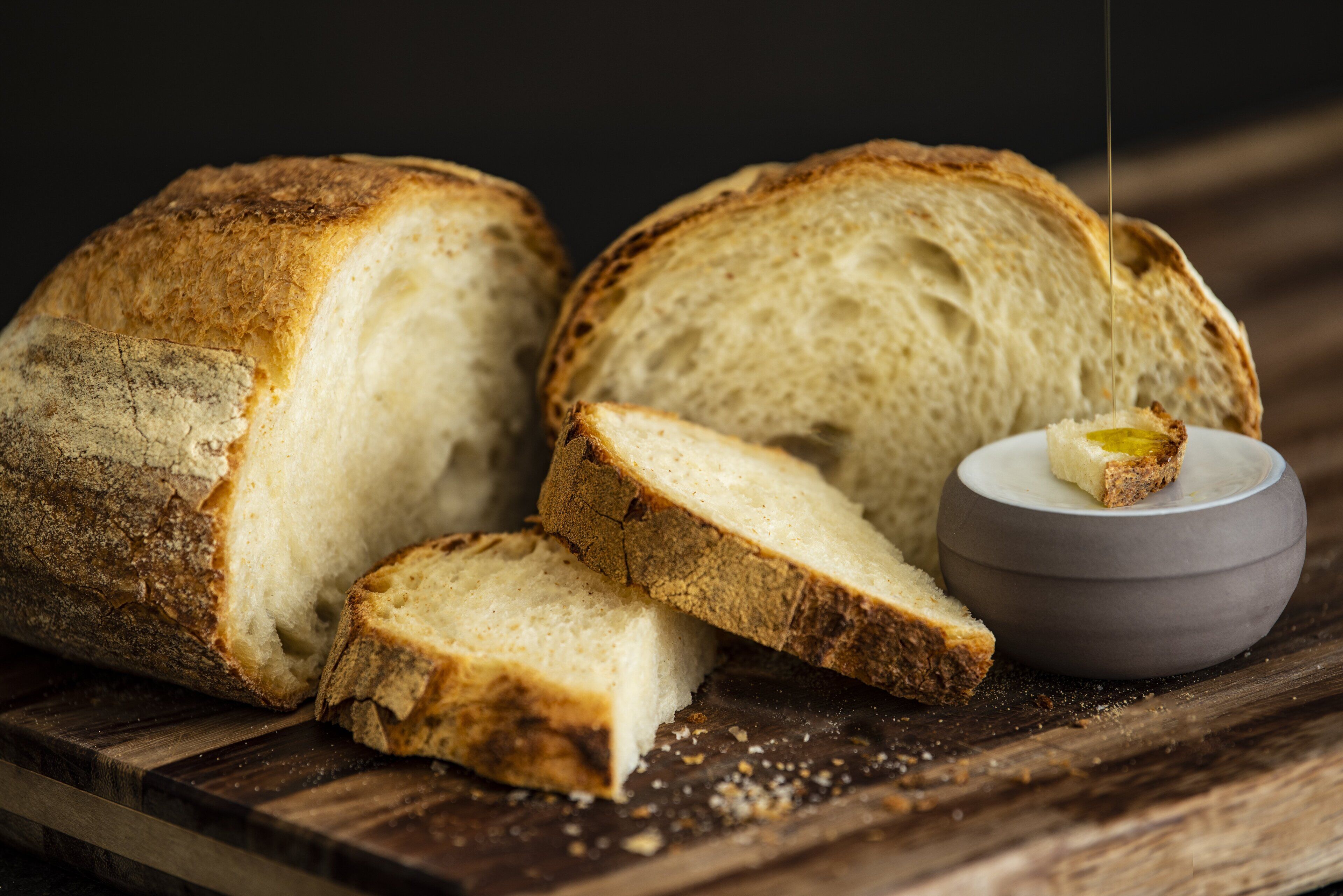 A loaf of bread with slices cut and a bowl of butter.