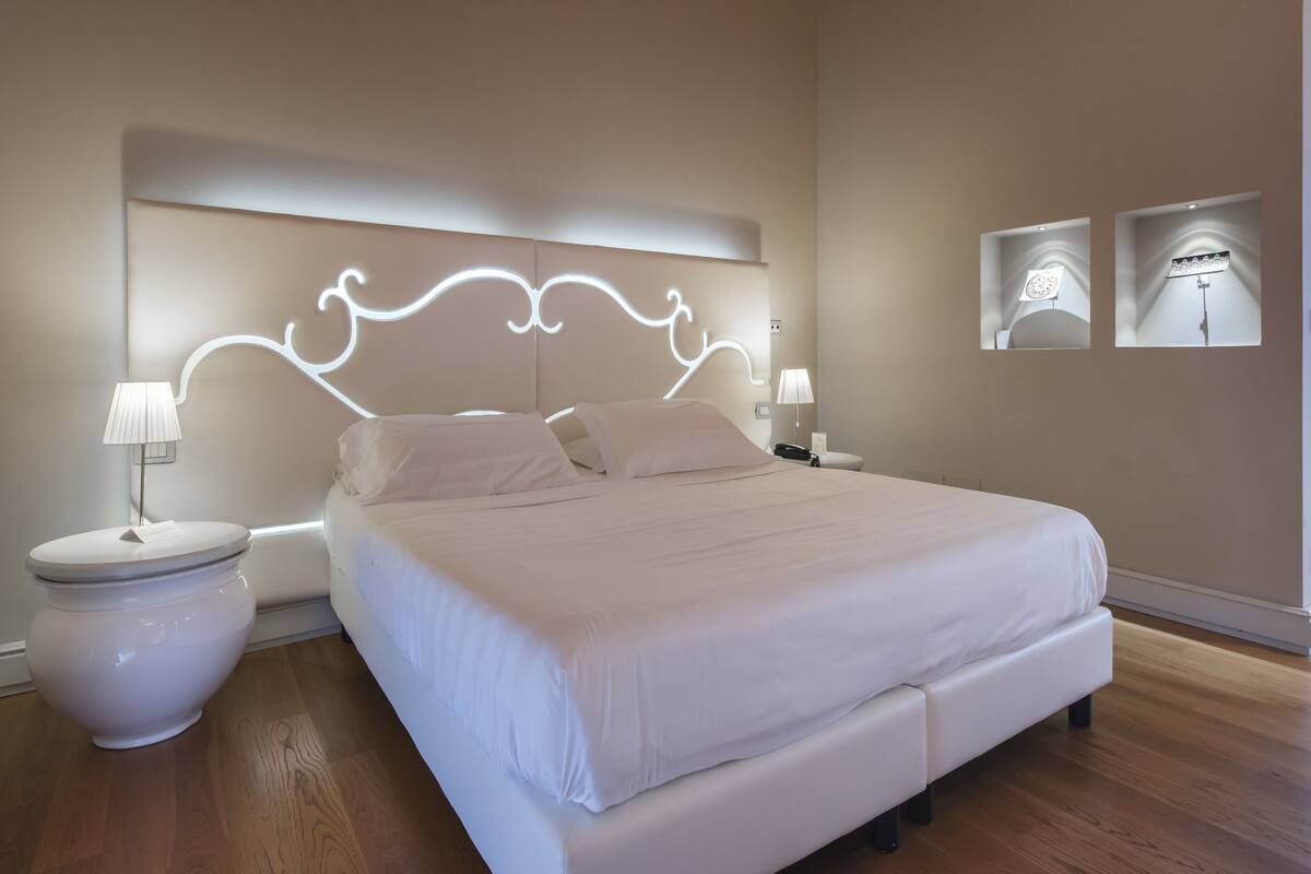 A modern bedroom with a large bed, bedside lamps, and a headboard with integrated lighting.