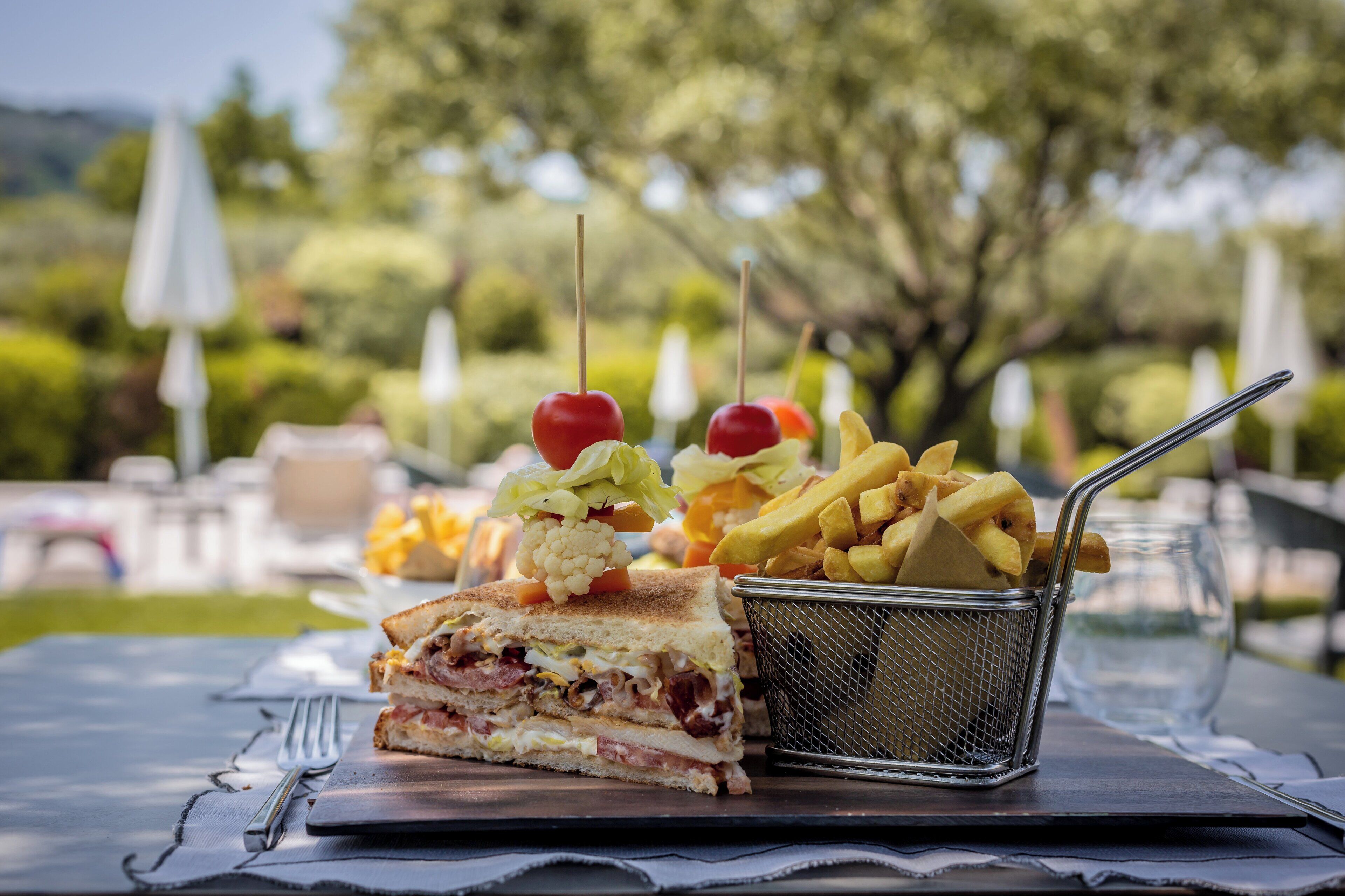 A meal consisting of a sandwich, fries, and a salad with cherry tomatoes on a table outdoors.