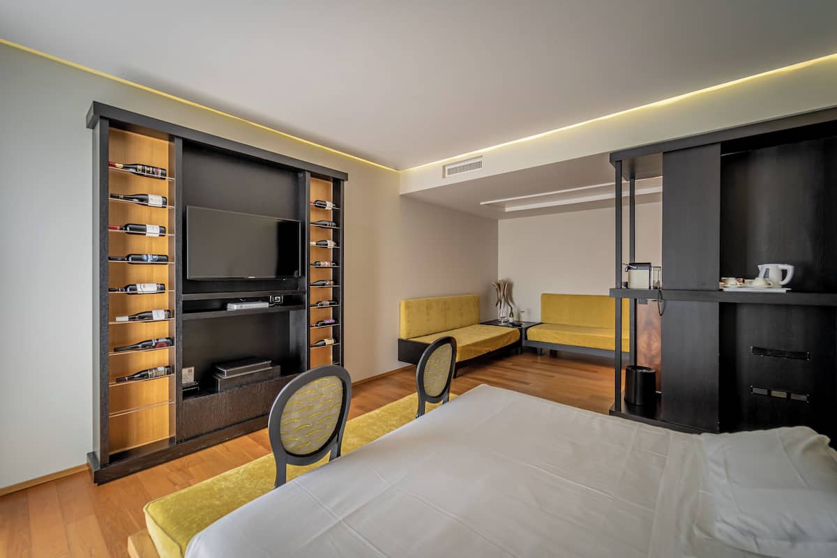 A modern hotel room with a large bed, a TV, a seating area, and a minibar.