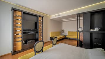 A modern hotel room with a large bed, a TV, a seating area, and a minibar.
