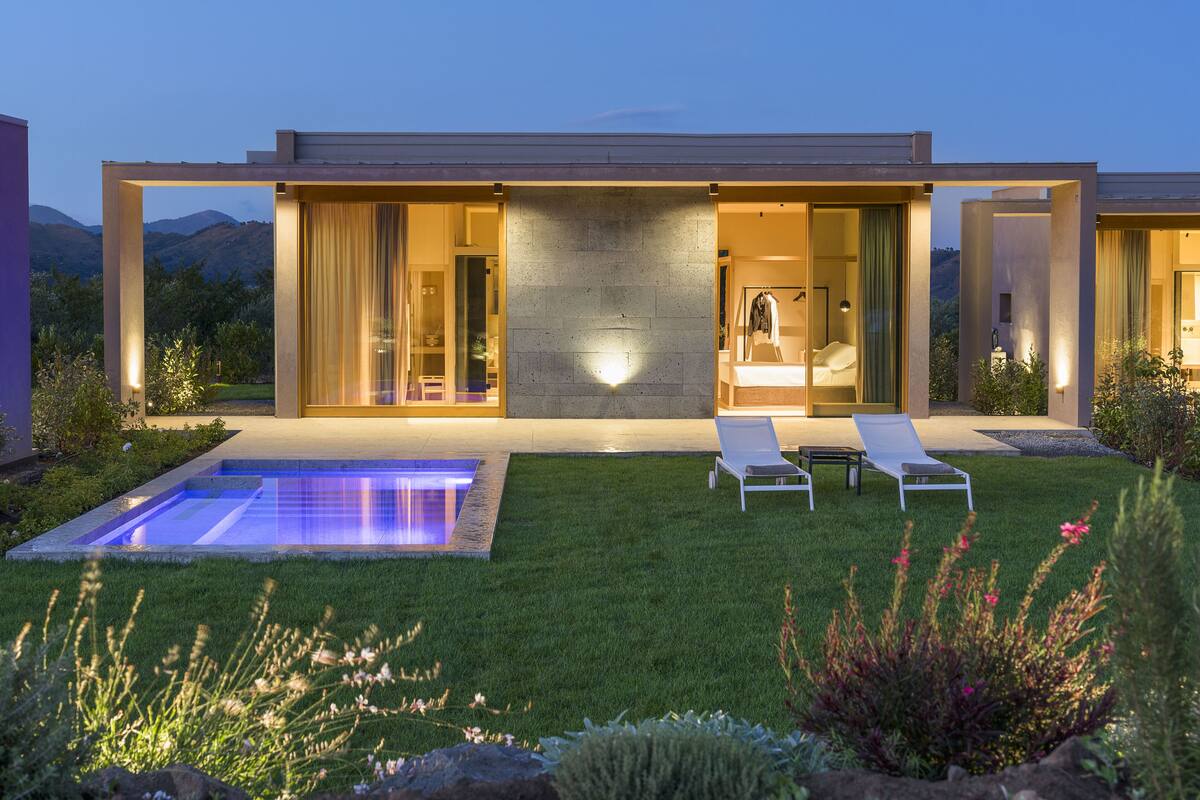 A modern house with a swimming pool, two lounge chairs, and a bathroom visible through the open doors.