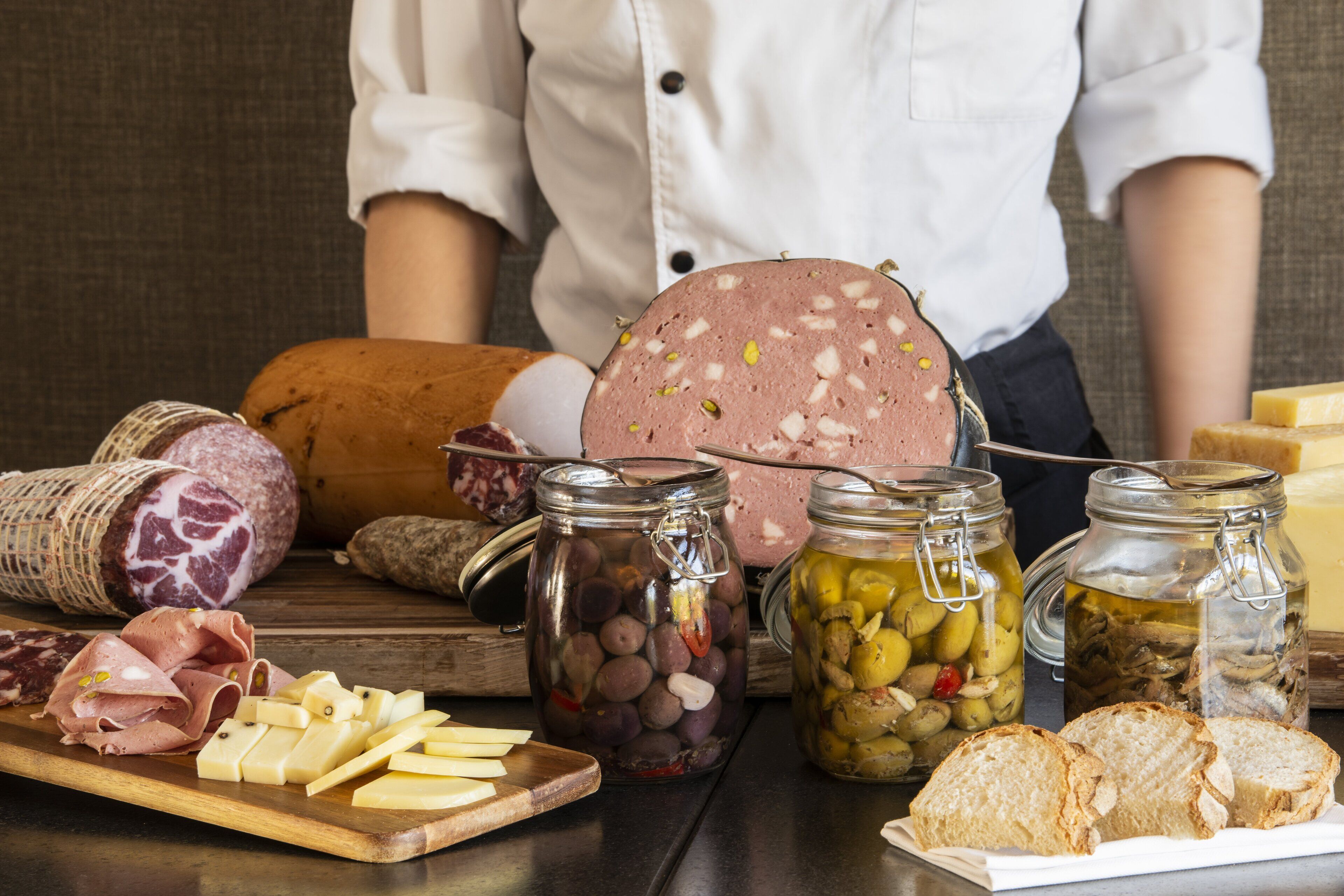 A variety of cured meats, cheeses, and pickled vegetables on a wooden board.