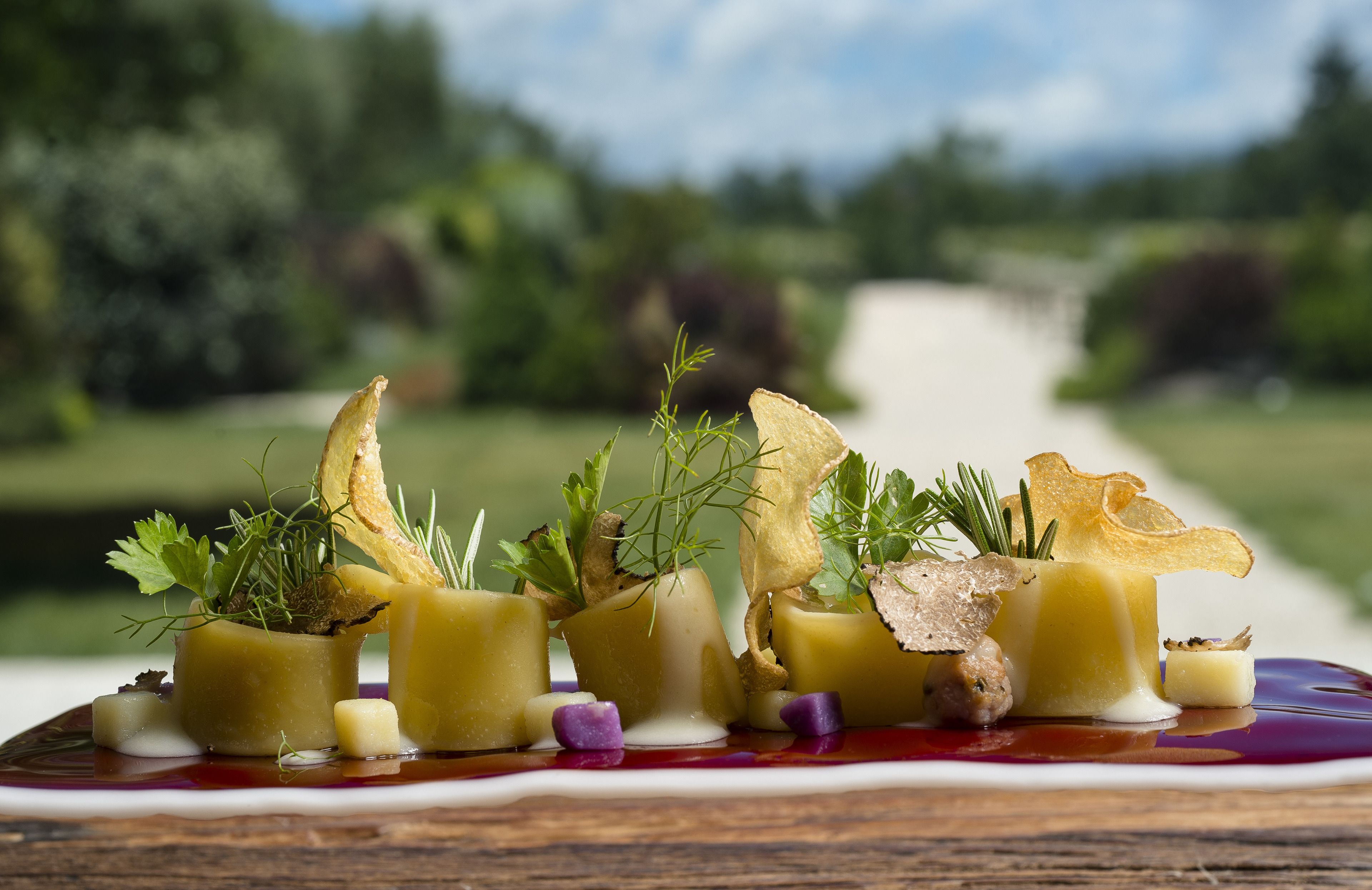 Un plato gourmet con diversos ingredientes y adornos sobre una mesa de madera.