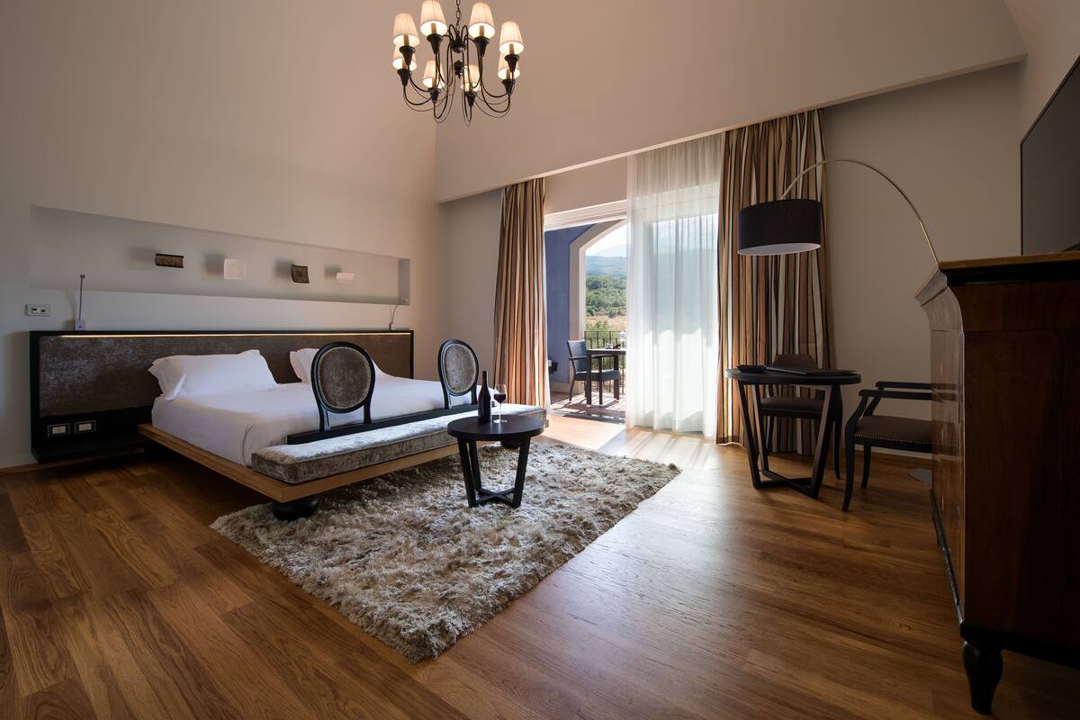 A modern hotel room with a bed, a desk, a chair, and a view of the outdoors.