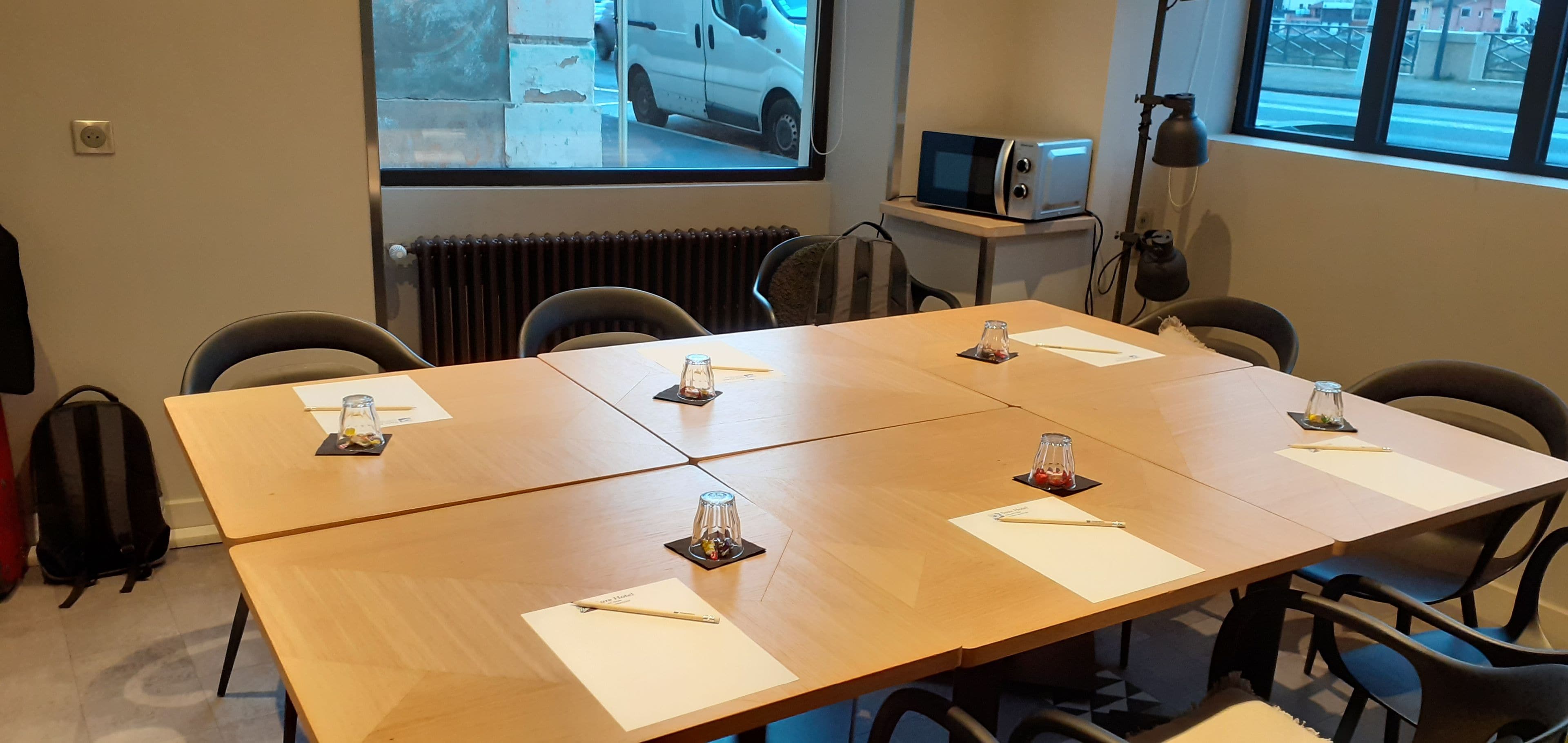 Una sala de conferencias con una mesa grande, cuatro sillas, una pantalla de proyector, un microondas y un ventanal con vista a la calle.