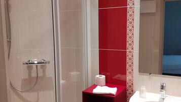 Une salle de bain moderne avec une douche à parois de verre, un mur d’accent rouge, un lavabo blanc et un miroir au-dessus.