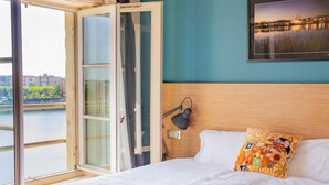 A hotel room with a bed, a desk, a chair, a lamp, and a view of a river. - Hotel du Nord (Mâcon)