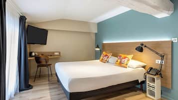 A hotel room with a bed, bedside table, lamp, and a desk with a chair.