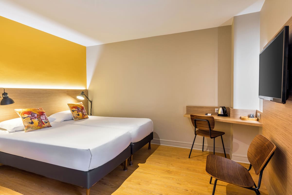 A hotel room with a bed, bedside table, chair, desk, and TV.