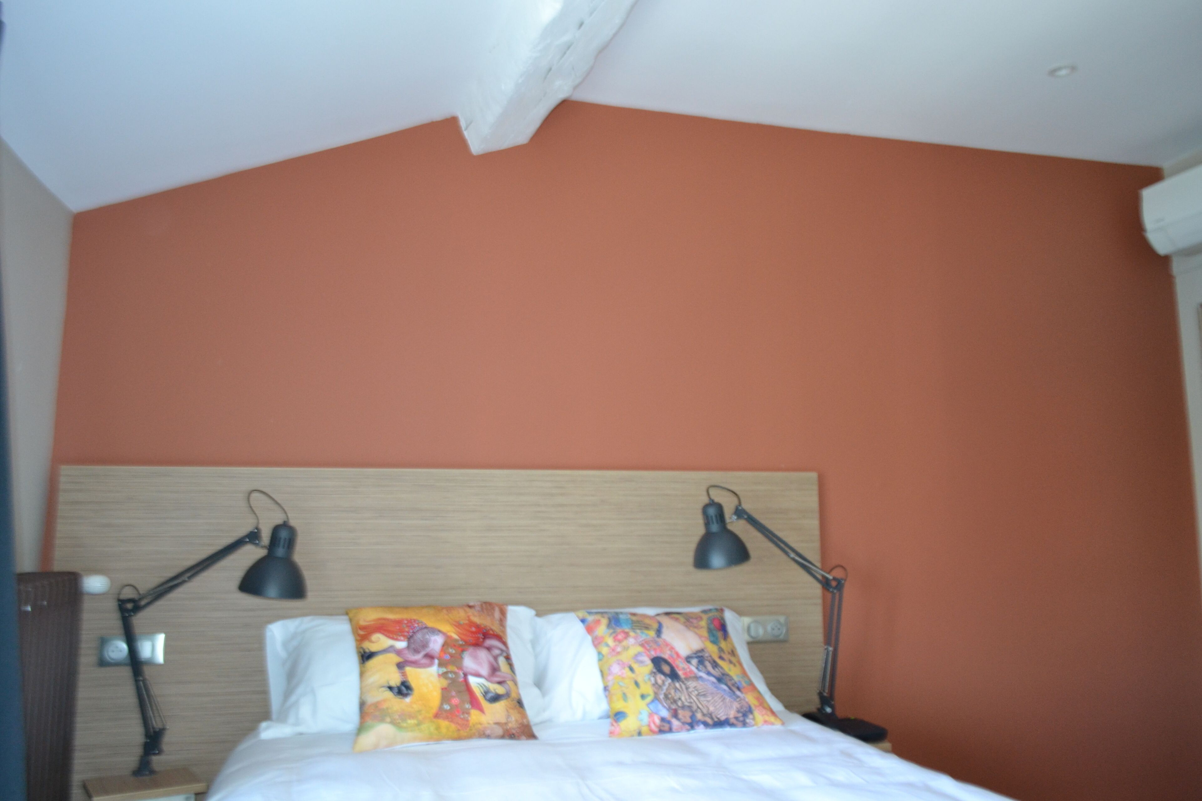 Een slaapkamer met een houten hoofdbord, twee bedlampjes en kleurrijke kussens.