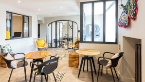 A modern interior with a round wooden table, black chairs, and a large window with a colorful butterfly decoration. - Hotel du Nord (Mâcon)