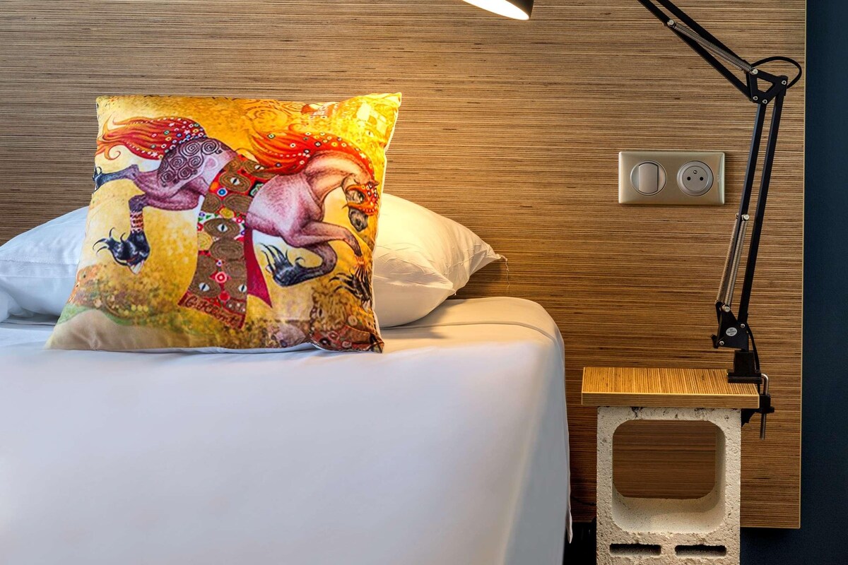 A bed with a colorful pillow, a black desk lamp, and a wooden headboard.