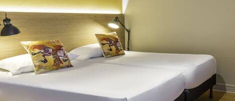 A double bed with white linens, two decorative pillows, a black floor lamp, and a wooden headboard.
