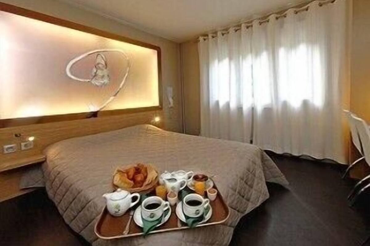 A hotel room with a large bed, a bedside table, a tray with breakfast items, and a window with curtains.
