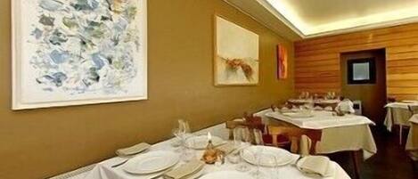 Un comedor con mesas dispuestas para una comida, obras de arte enmarcadas en las paredes y una decoración interior cálida.