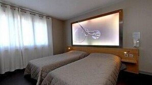 Una habitación de hotel con dos camas individuales, un espejo grande y una mesita de noche con una lámpara.
