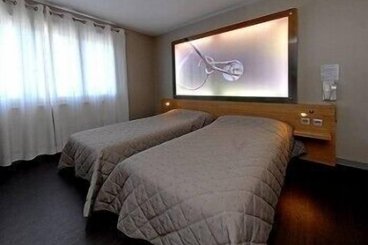 A hotel room with two single beds, a large mirror, and a bedside table with a lamp.