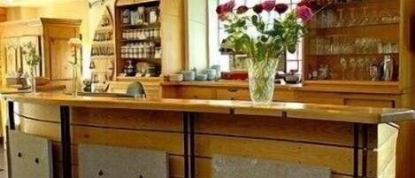 A bar area with wooden cabinets, a vase with flowers, and a window with blinds.
