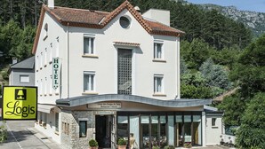 Un hotel con fachada de piedra, entrada a un restaurante y vista de una zona montañosa.