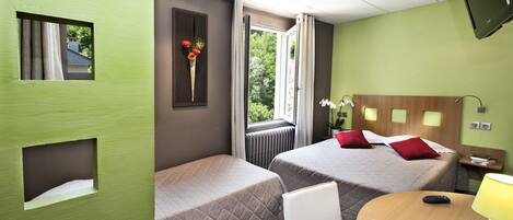 Una habitación de hotel con dos camas, una ventana con cortinas, un televisor y una pequeña mesa con lámpara.