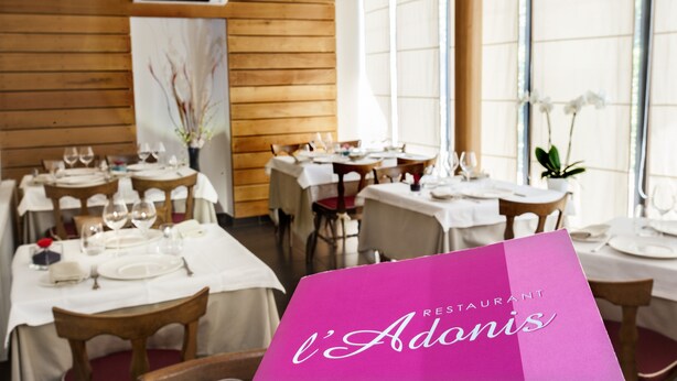 Interior de restaurante con varias mesas dispuestas para comer, paredes de paneles de madera y grandes ventanales.