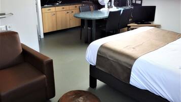 A hotel room with a bed, a desk, a chair, a sofa, a small round table, and a kitchenette in the background.
